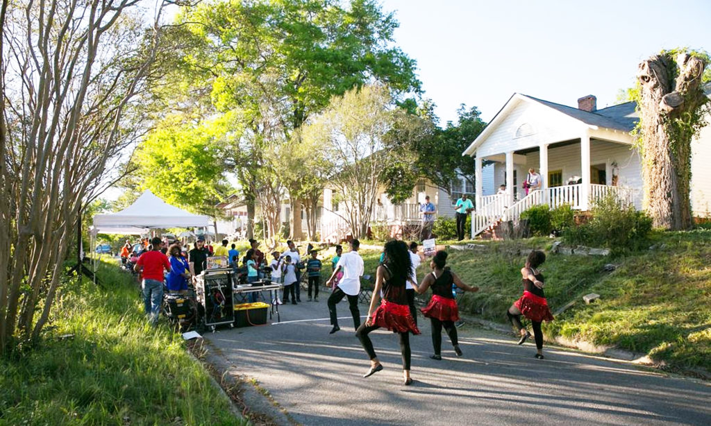 A group of children dancing and people at a community event in front of a building in East Macon Arts Village.