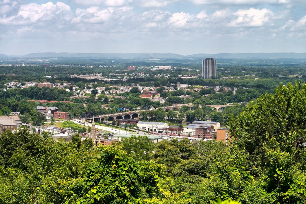 Photography of the Lehigh Valley, with trees in the foreground and a small city in the background.
