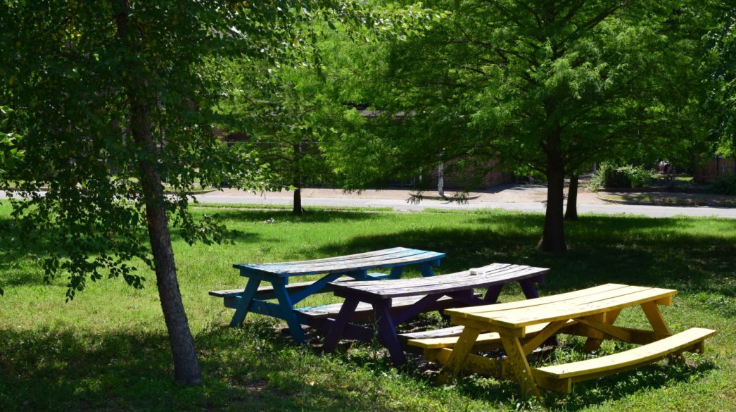 A blue, purple, and yellow picnic table in a row in a park.