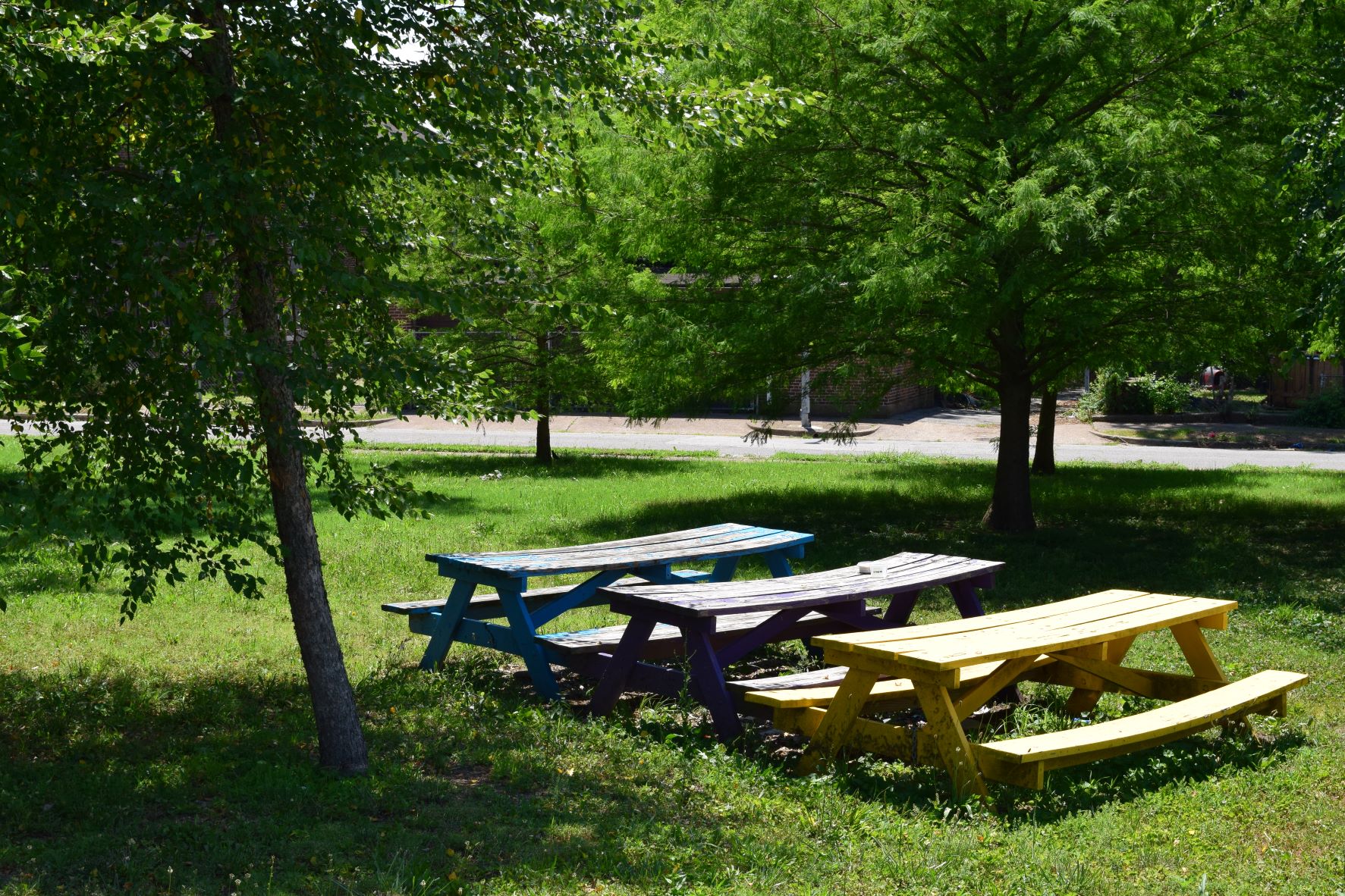 A blue, purple, and yellow picnic table in a row in a park.