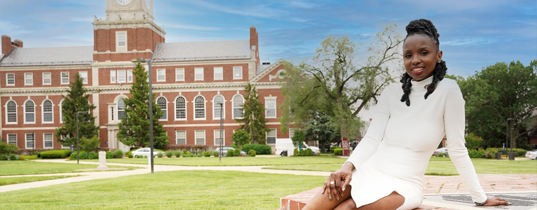 Kat Guillaume-Delemar sits, smiling, in a white dress in front of Howard University.