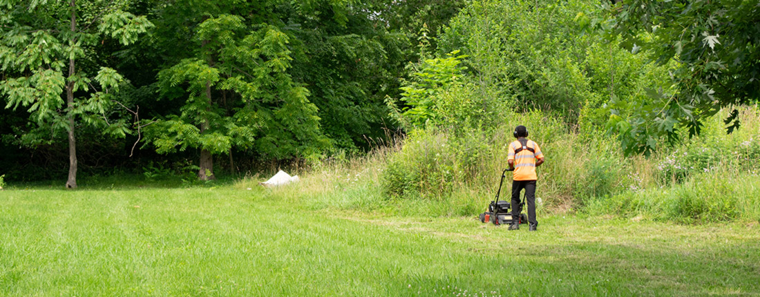 A person in a reflective orange vest mows a vacant lot.