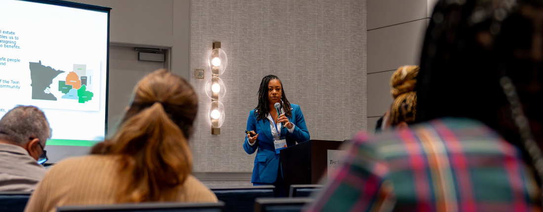 A photo from the 2025 NLBN Summit. A woman delivers a presentation to a packed conference session.