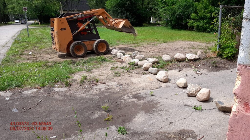 A bulldozer moves small boulders into place as a barrier on a vacant lot.