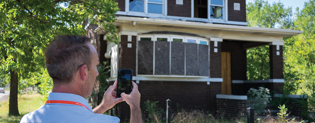 Man taking a photo of an abandoned boarded up home