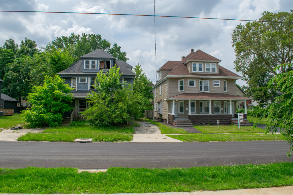 Two homes in Cleveland that look of identical construction except the one on the left has clearly been abandoned, with broken windows and overgrown plants, and the one on the right looks recently renovated and is currently for sale.