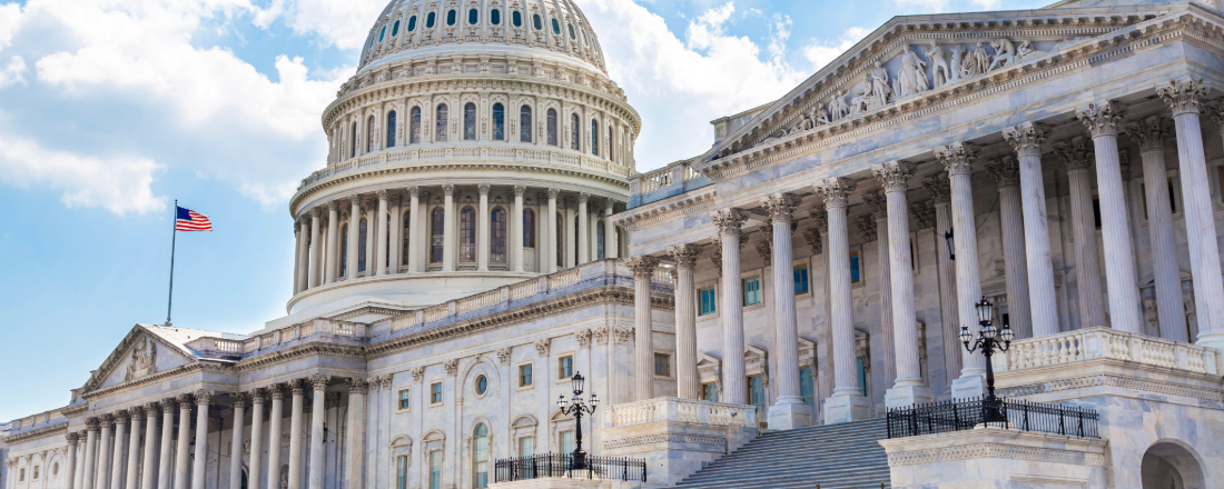 An image of the US Capitol building on a sunny day, with the American flag flying in the breeze.